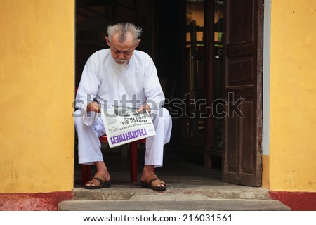 HOI AN - APIRL 18, 2014. Elderly chinese man reading newspaper in the street in front of his shop