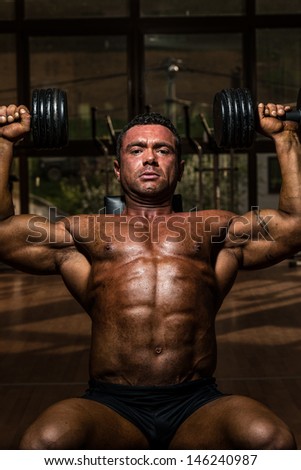shirtless bodybuilder doing shoulder press whit dumbbell