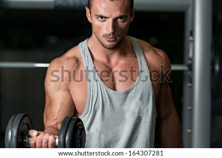 Man In The Gym Exercising Biceps With Dumbbell. Young Athlete In Gym Exercising With Dumbbell