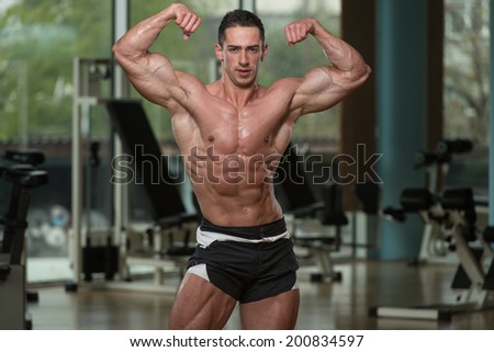 Muscular Men Is Hitting Rear Double Biceps Pose - Serious Man Standing In The Gym And Flexing Muscles