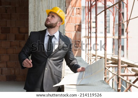 Young Construction Worker In Hard Hat - Portrait Of Construction Master With Yellow Helmet And Blueprint In Hands
