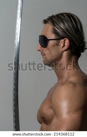 Warrior With Long Sword Over Grey Background - Portrait Of A Handsome Muscular Ancient Warrior With A Sword
