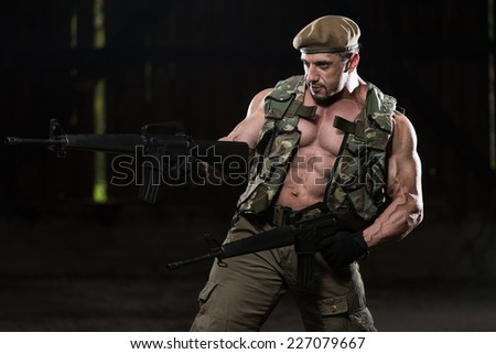 Action Hero Muscled Man Holding Machine Guns - Standing In Abandoned Building Wearing Green Pants