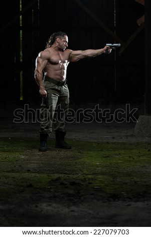 Action Hero Muscled Man Holding A Gun - Standing In Abandoned Building Wearing Green Pants