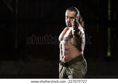 Action Hero Muscled Man Holding A Gun - Standing In Abandoned Building Wearing Green Pants