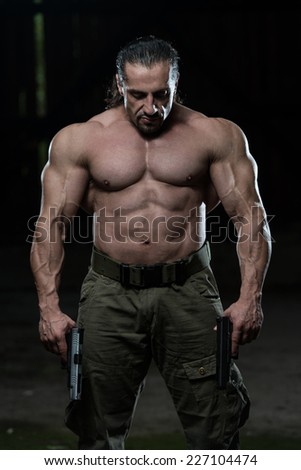 Muscular Man Holding Guns - Standing In Abandoned Building Wearing Green Pants
