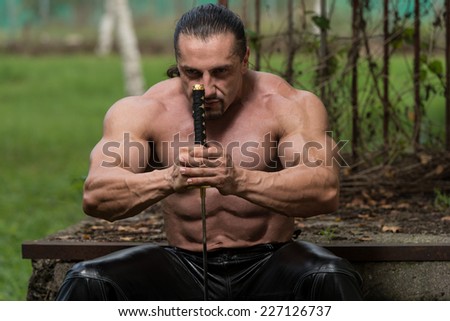Strong Man With Samurai Sword - Standing In Forest Wearing Leather Pants