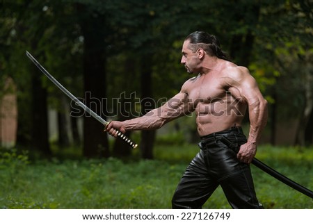 Man Drawing Ancient Sword In Self Defense - Standing In Forest Wearing Leather Pants