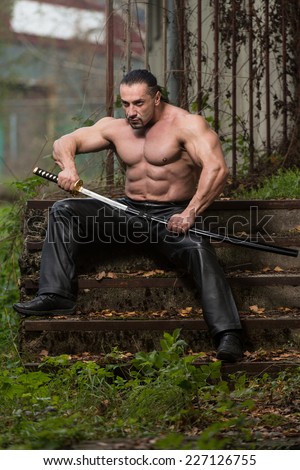 Portrait Of A Muscular Ancient Warrior With Sword - Standing In Forest Wearing Leather Pants