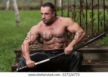 Portrait Of A Muscular Ancient Warrior With Sword - Standing In Forest Wearing Leather Pants