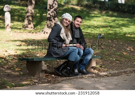 Couple Reading A Book - Relaxed Young Couple Reading Book In Park Bench