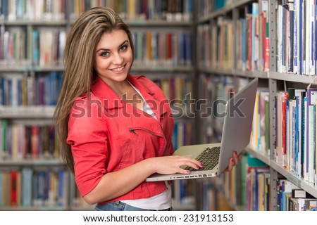 In The Library - Pretty Female Student With Laptop And Books Working In A High School - University Library - Shallow Depth Of Field