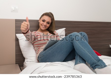Young Female Student Lying On Bed And Having Fun With Touch Pad In Bedroom