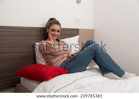 Young Female Student Lying On Bed And Having Fun With Touch Pad In Bedroom