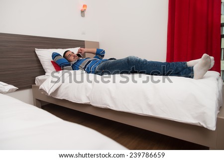 Young Man Lying On Bed And Having Fun On Phone In Bedroom