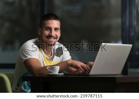 Young Male Student Drinking And Having Fun With Laptop In Cafeteria