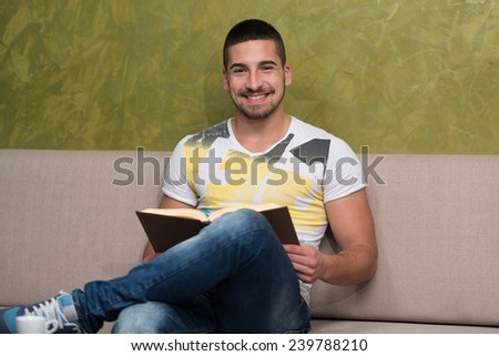 Young Male Student Drinking And Reading Book In Cafeteria