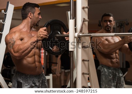 Body Builder Putting Weights On Bar In Gym