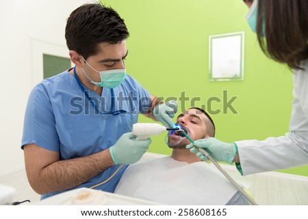 Male Patient With Dentist And Assistant In A Dental Treatment - Wearing Masks And Gloves