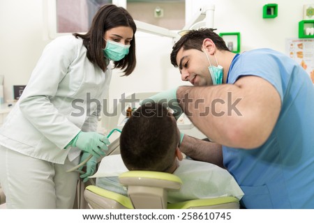 Male Patient With Dentist And Assistant In A Dental Treatment - Wearing Masks And Gloves