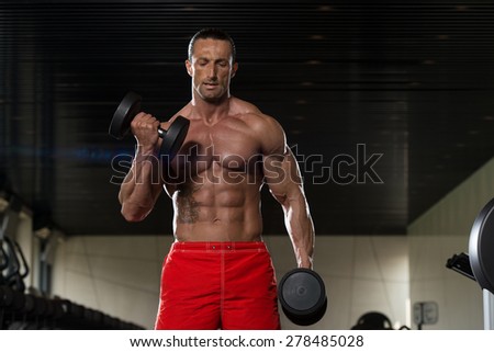 Muscular Mature Man Doing Heavy Weight Exercise For Biceps With Dumbbells In Modern Fitness Center