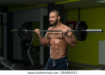 Muscular Young Man Doing Heavy Weight Exercise For Biceps In Gym