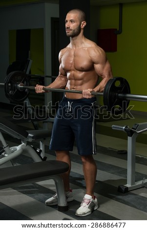 Muscular Young Man Doing Heavy Weight Exercise For Biceps In Gym