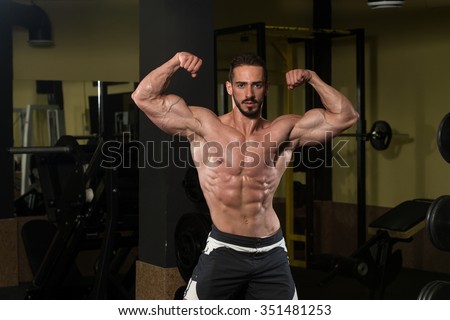 Serious Man Standing Strong In The Gym And Flexing Muscles