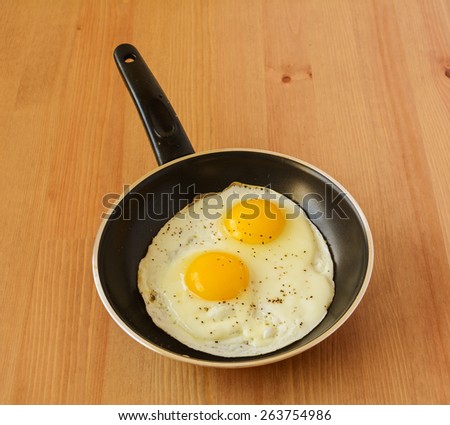 A pair of eggs prepared as sunny side up and sprinkled with pepper in a saucepan