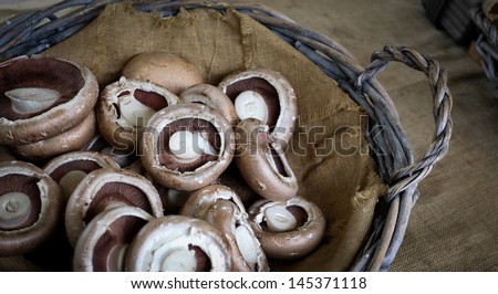 Brown champignons in grey basket with jute bag on rustic table cowered with jute