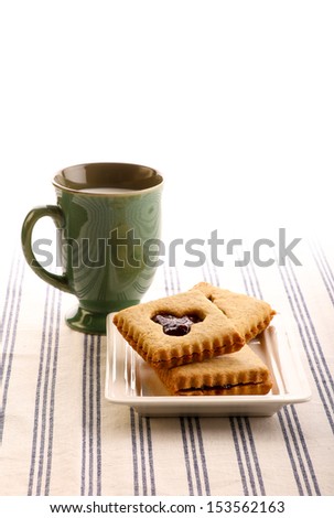 Hazelnut biscuits cookies with mixed berry jam on white plate and milk mug on striped tablecloth