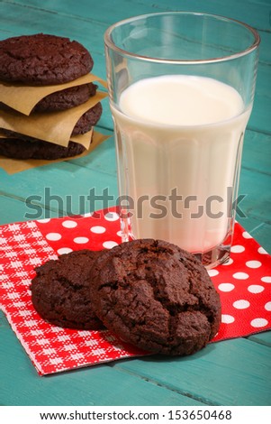 Dark chocolate cookies with milk in glass, red dotted napkin and turquoise rustic table