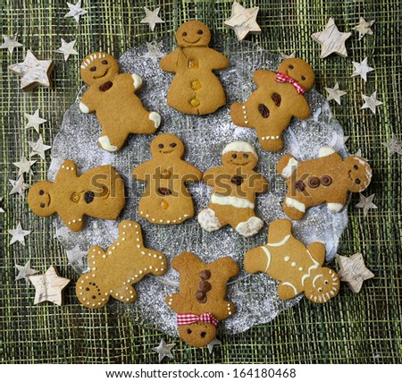 Happy Gingerbread cookies on glass plate dancing in the circle with gingerbread couple in the middle, icing sugar on glass plate, green straw background