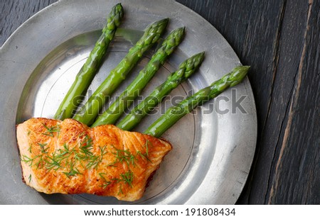 Salmon fillet with asparagus and chives on old tin plate dark rough wood