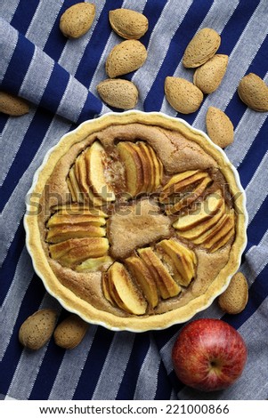 French apple tart sweet cake in white desert pie backing tray on blue striped cloth and whole almonds