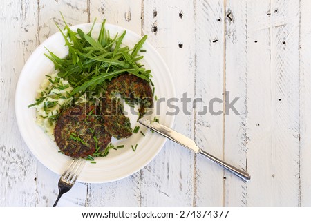 Swiss chard veggie fritters with mash potatoes and rocket leaves on white plate, fork and knife and white rough background, copy splace