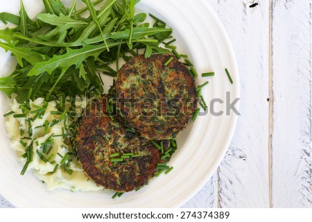 Swiss chard veggie fritters with mash potatoes and rocket leaves on white plate and white rough background, copy splace