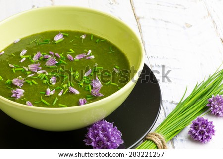 Swiss chard and potato cream soup with chopped chives with edible chives flowers in green ceramic bowl