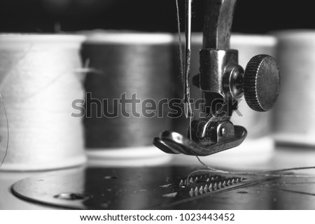Old sewing machine with colour thread and needle, on a old grungy work table. Tailor\'s work table. textile or fine cloth making. industrial fabric black and white