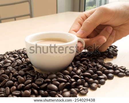 a women hand holding a cup of coffee and many coffee beans on the wooden table