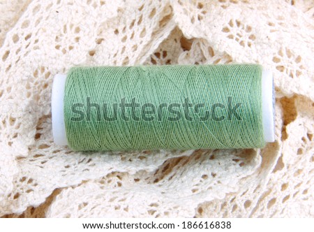 Green cotton thread bobbin on cream lace.