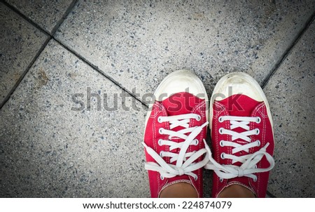 Feet in red canvas sneaker on concrete floor, top view