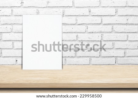 White poster on wood table and white brick wall, template background