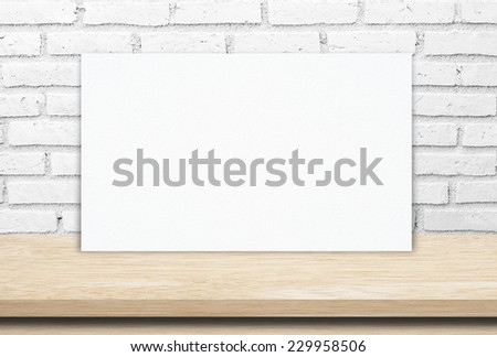 White poster on wood table and white brick wall, template background