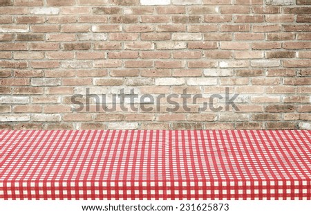 Empty table covered with red checked tablecloth over brick wall background, for product display montage
