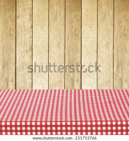 Empty table covered with red checked tablecloth over vintage wooden wall background, for product display montage