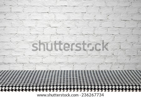 Empty table covered with black and white checked tablecloth over white brick wall background, for product display montage