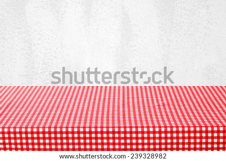 Empty table covered with red checked tablecloth over white cement wall background, for product display montage