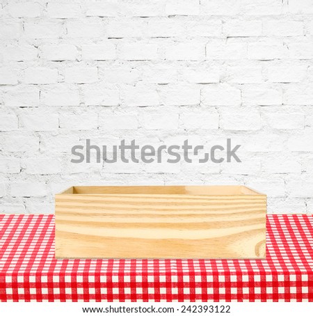 Wooden storage box on table covered with red checked tablecloth over white brick wall background, for product display montage background