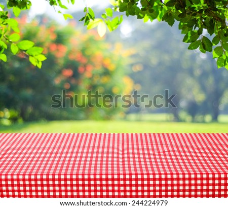 Empty table and red tablecloth with blur green leaves bokeh background, for product display montage